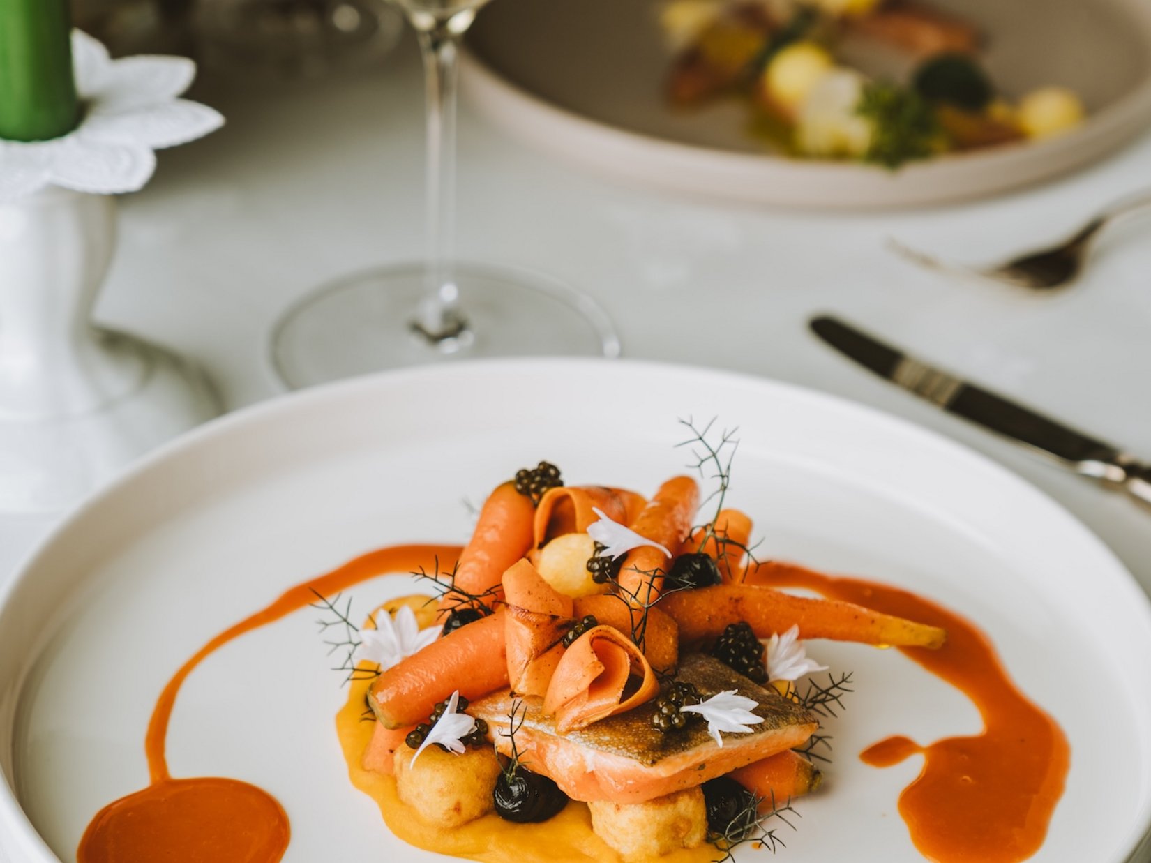 Impressions Gourmet dish with carrots and sauce on white plate, white wine in background