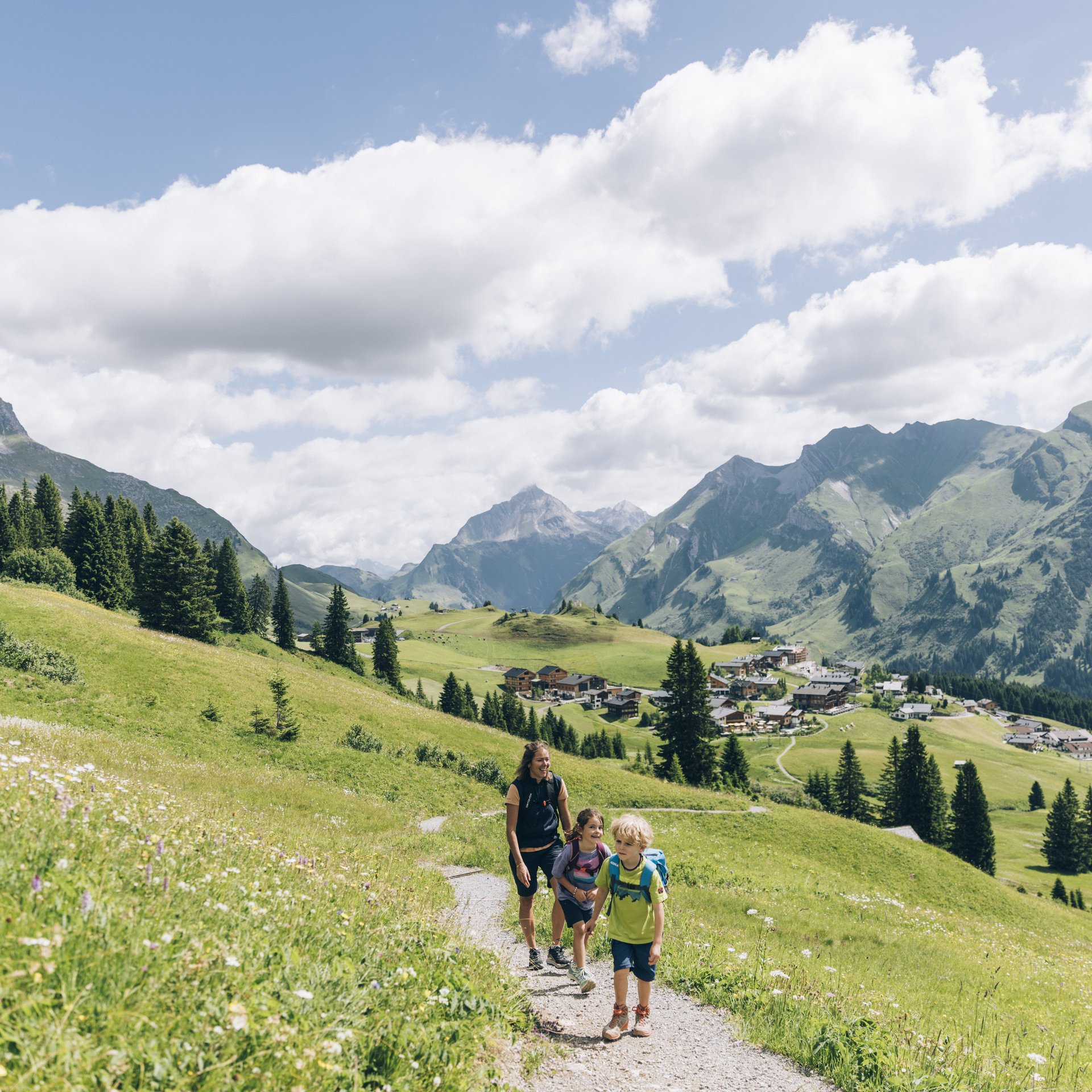 Sommer am Arlberg | Alpine Natur, Bewegung & Erholung im Hotel Post Lech Familie wandert auf einem Bergweg mit Alpenlandschaft und blauem Himmel