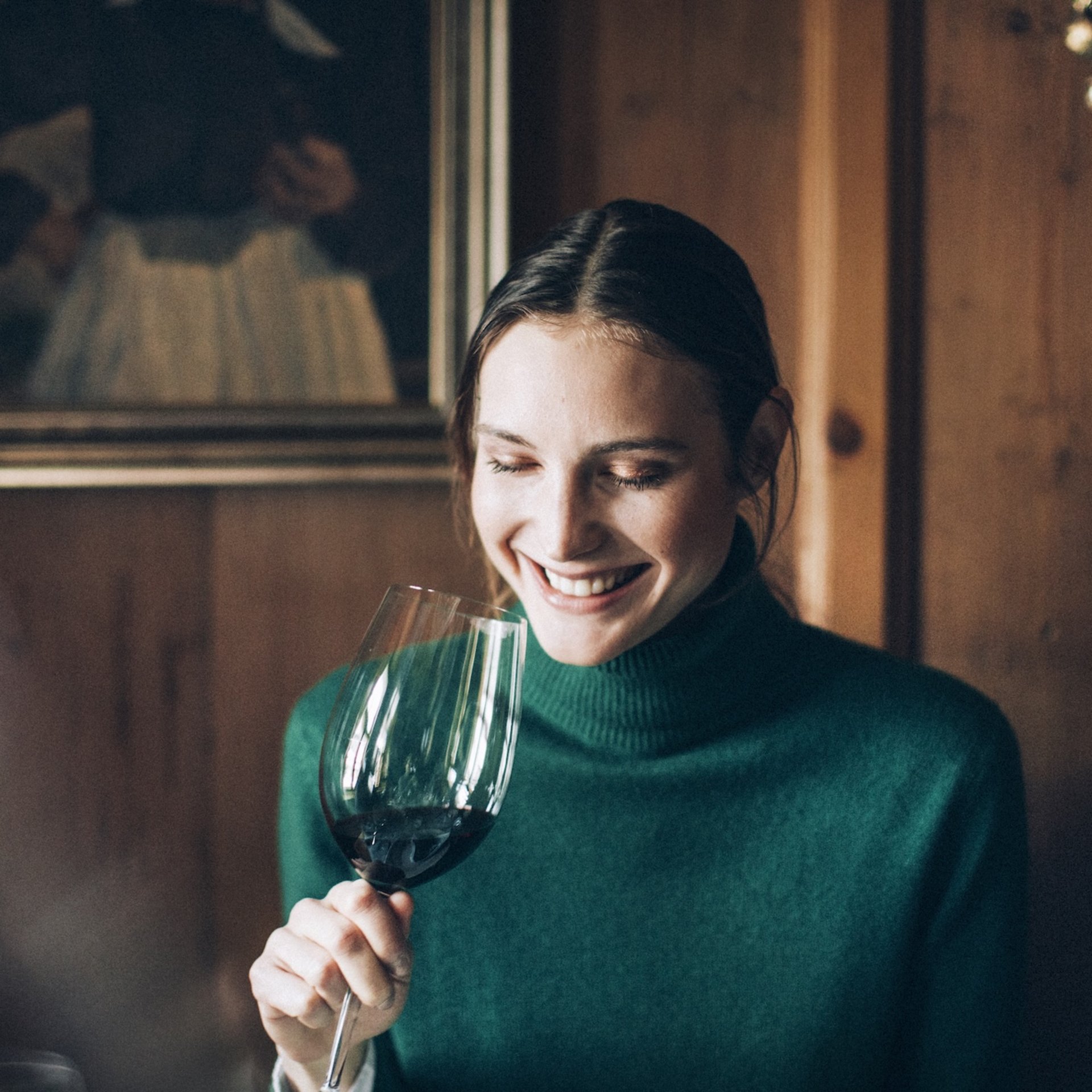 Veranstaltungen Frau in grünem Pullover lächelt und hält ein Glas Rotwein