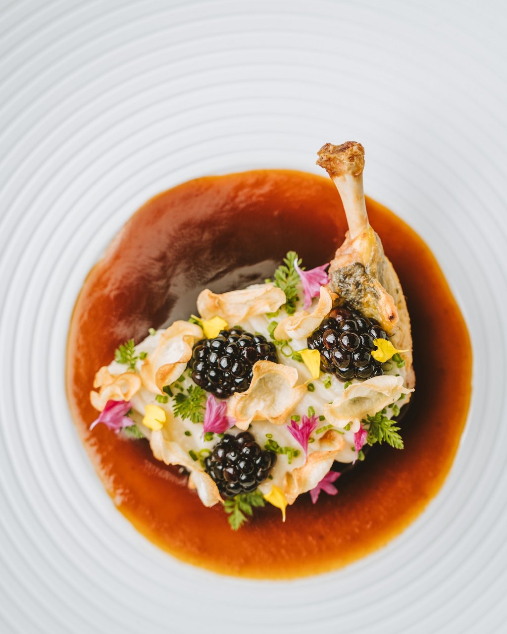 Hotel Gasthof Post in Lech am Arlberg Gourmet-Geflügelgericht mit Sauce und essbaren Blumen auf weißem Teller