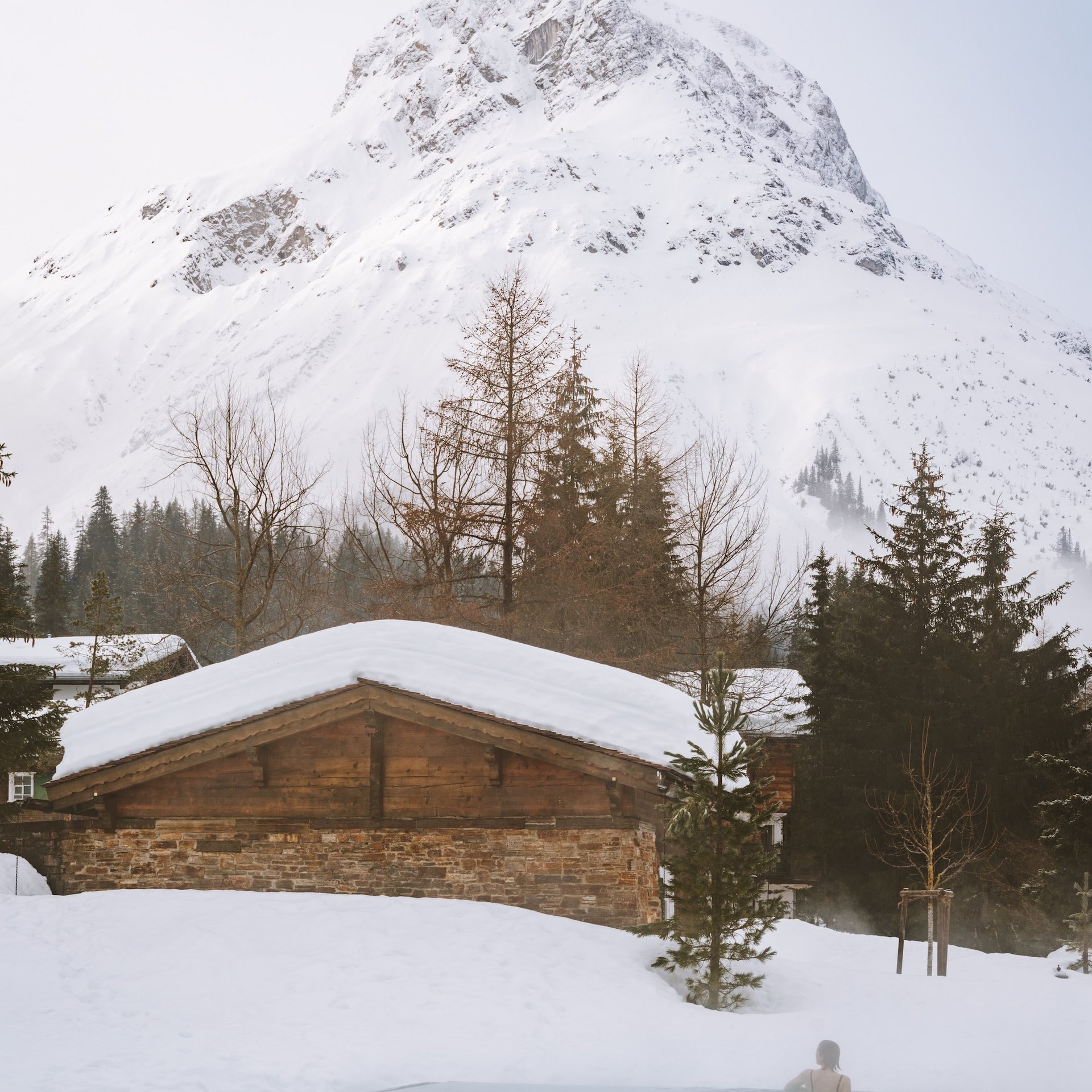 Winter Holidays in Lech at the Arlberg | Skiing, Relaxation & Luxury at Hotel Post Lech Person relaxing in outdoor pool with snowy mountains in the background
