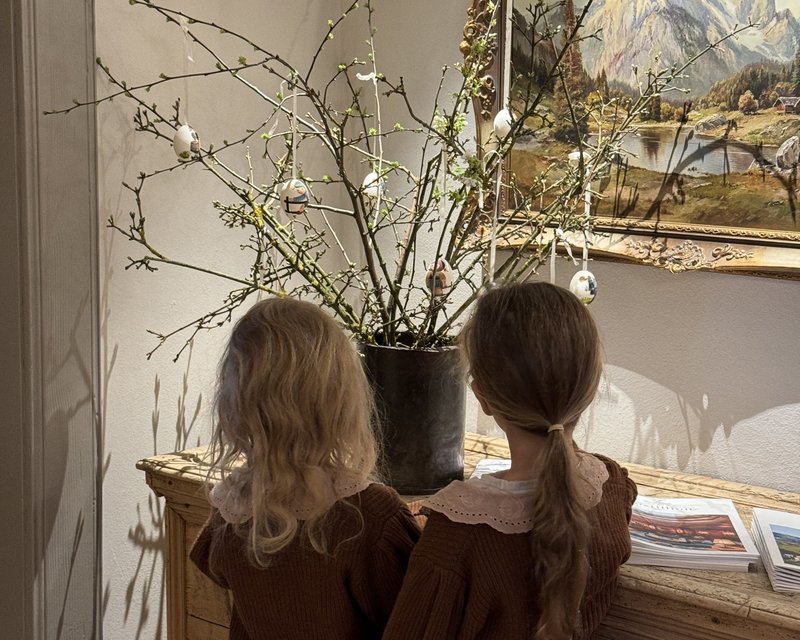 Neues aus der Post Zwei Kinder schauen auf einen Holztisch mit blühenden Ästen und bemalten Ostereiern