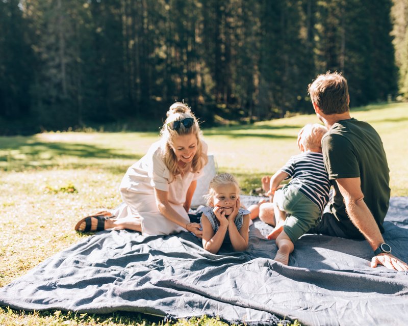 Neues aus dem Hotel Post Lech Familie mit zwei Kindern entspannt auf einer Decke im sonnigen Park