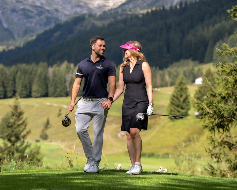 Neues aus dem Hotel Post Lech Paar beim Golfspielen in den Bergen hält Händchen und lächelt sich an