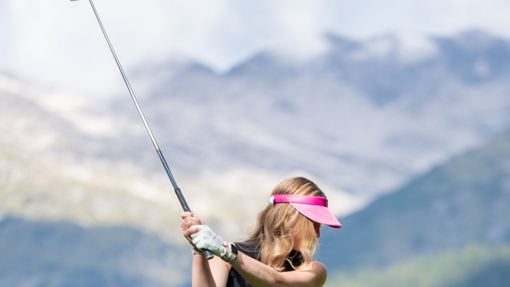 Golf Unlimited Woman wearing pink visor hitting a golf ball on a course with mountain background